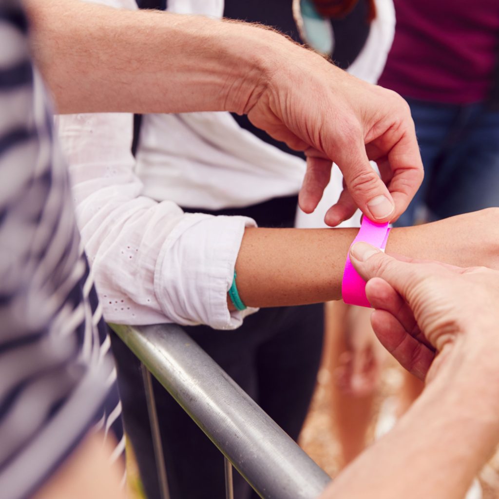 A person is putting on a pink paper wristband to mark the attendees entrance at an event.